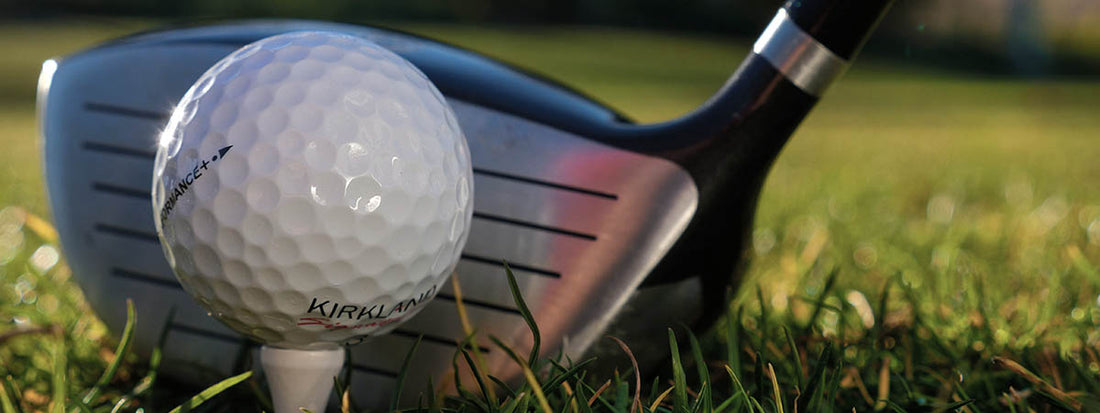 Golf ball on a tee with a golf club in the background on grass