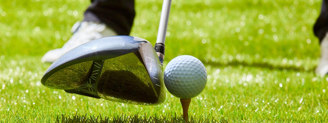 Golf club hitting a ball on a tee with grass in the background