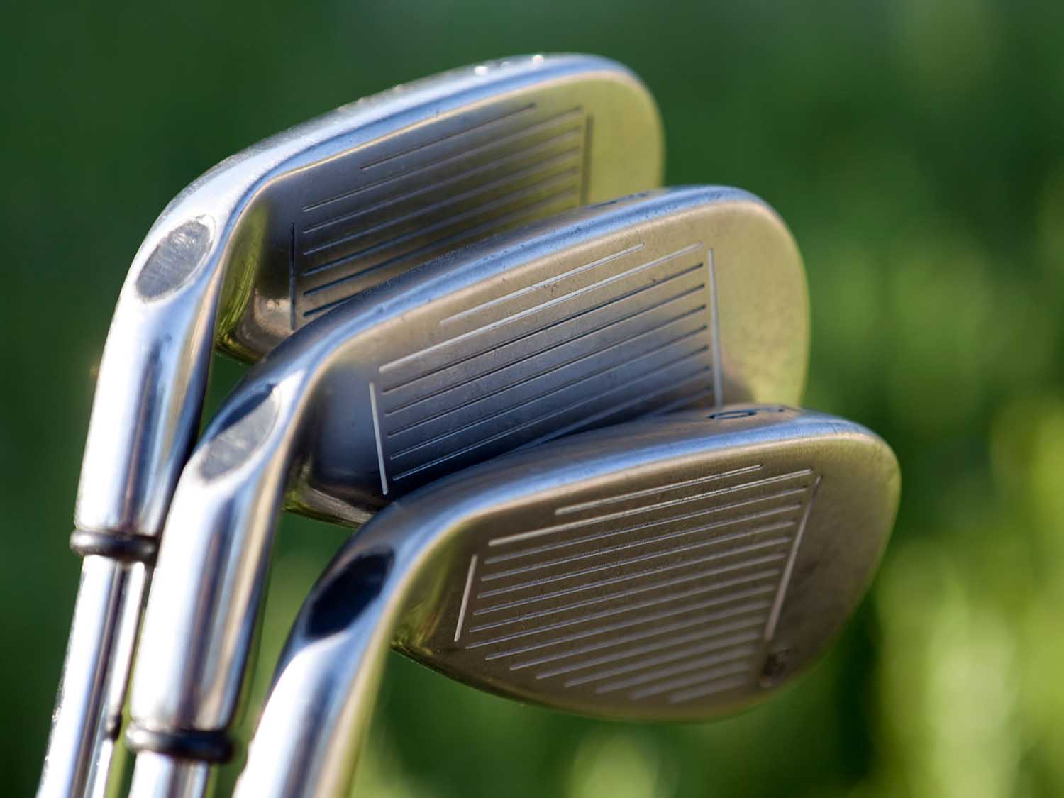 Close-up of three golf clubs with a blurred green background