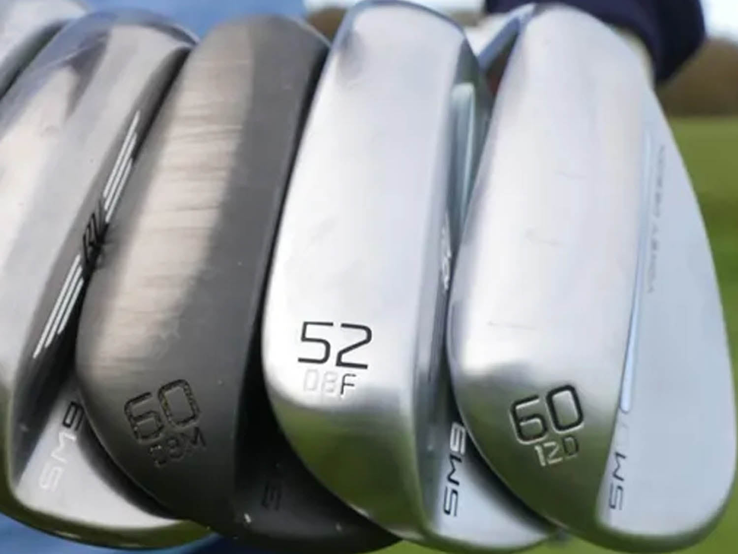 Close-up of golf club heads with different degrees of loft on a blurred background