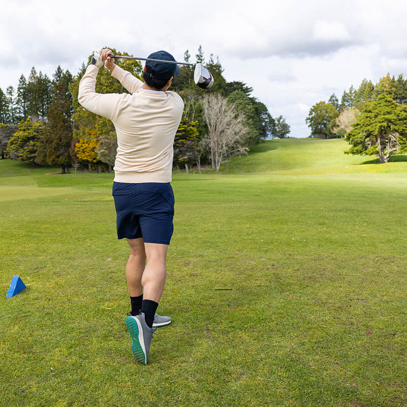 Person playing golf on a green course in new zealand with trees in the background
